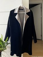 Full view of the black knit cardigan with grey/beige lining, hanging on a hanger showing the full garment.