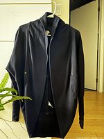 Front view of black cardigan hanging showing shawl collar, relaxed fit, long sleeves, and pockets.