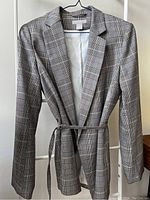 Front view of plaid blazer hanging on a hanger, showing full length and belt tied at the waist.