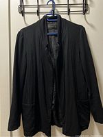 Black Zara Basic casual cardigan on a blue hanger against a wall, displaying front view with open front and two pockets.