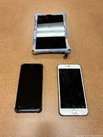 Devices laid out on a carpet surface showing front screens: tablet in colorful case, black smartphone screen off, white iPhone with cracked screen