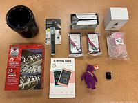 All assorted items arranged on table including KitchenAid canister, measuring spoon, Diaper Genie bags, e-Writing board, massage balls, toys, light clips and plug