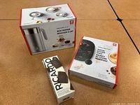 Photo of Zwilling Enfinigy milk frother box, digital kitchen scale box, and a Ricardo chocolate bar mold box on table.