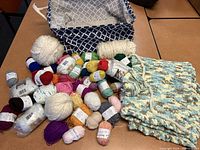 Photo showing assortment of yarn skeins in various colors and sizes with a woven blue, white, and brown blanket