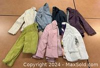 Seven Danier leather jackets of various colors laid out on a table.