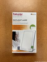 Front box view showing the brand, product name, and image of the lamp with a person resting next to it.