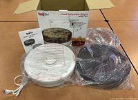 Photo showing all components of the food dehydrator including base unit, stackable trays, box and instruction manual, all wrapped in protective plastic.