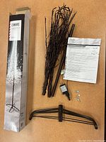 Full view of contents including boxed product, multiple twig branches with embedded lights, metal tripod stand, instruction manual, and electrical plug