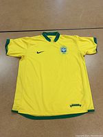 Full front view of yellow soccer shirt with green collar and sleeve edges, showing embroidered Brazil crest and black Nike swoosh logo.