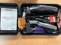 Wahl pet clipper kit items inside black plastic storage case showing clipper, trimmer, guide combs, charger, cleaning brush, oil, and instruction manual.