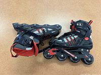 Pair of black and red rollerblades viewed from above on a brown surface.