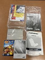 Collection of user manuals including Sony PlayStation game manual, Paramount parking sensor manual, Samsung Blu-ray player manual, TV game manual and Toshiba TV manual, some wrapped in plastic.