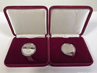 Two 1982 Canadian dollar coins in red velvet boxes with cream satin lining, front view, both coins sealed in clear capsules.