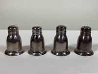Front view of four Birks sterling silver shakers standing side by side on white background. Slender with slightly wider bases and hole patterns on tops.