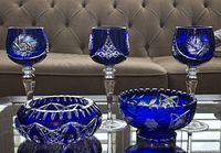 All five pieces together including three blue crystal hock wine glasses with decorative cut patterns, a small footed serving bowl with sawtooth rim, and a smaller bowl or ashtray.