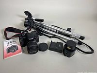 Overview of all included items on table: camera with lens, tripod, tele conversion lens, charger, manual, and caps