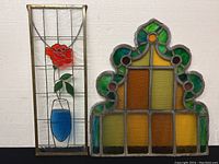 Photo of two stained glass wall panels shown side by side on a white background wall.