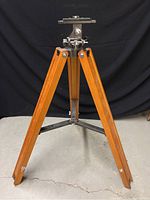 Full view of vintage wooden tripod with Vixen branded adjustable metal mount on top, against black backdrop