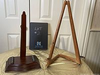 Two art display stands side by side: dark wood 22-inch tall stand with curved base and a light wood 18-inch tall A-frame easel stand.