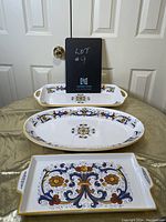 Front view of the three Bowring serving trays arranged on a gold cloth with floral and scroll decoration with gold trim.