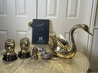 Front view of entire brass animal assortment showing swan, lion bookends, dog, and enamel duck on fabric surface with doors in background