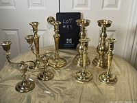 Overall view of eight vintage brass candle holders in different styles for pillar and taper candles, displayed on fabric.