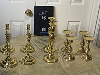 Full view of all eight brass candle holders arranged on a beige cloth, including taper and pillar styles, highlighting variety in height and design.