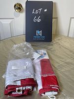 Two folded Canadian flags on a table: one nylon with label showing Canadian flags dimensions and material, and one heavier fabric flag with grommets and rope.