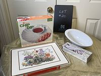 Photo showing all items in the lot: boxed 2-piece chip and dip bowl, white oval serving bowl, floral spoon rest, and floral placemats stacked.
