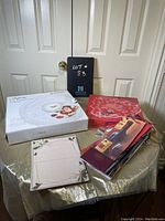 Photo of boxed Studio Nova Christmas plate, glass chip and dip bowl, Christmas wine gift bags, and floral writing paper on table.