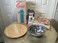 Overview of the lot showing the wooden lazy susan, stainless steel bowls, ceramic salsa and dip bowl, ceramic wine cooler, and boxed Airpot coffee pot.
