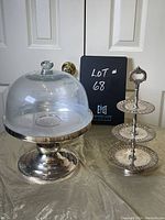 Silver plate cake stand with glass dome and 3-tier cupcake server shown on a table with a closed door in background.