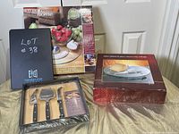 Full view of the Sarah Peyton Home glass lazy Susan box, cheese knife set in plastic packaging, and silver plated cheese board in original boxes on a table against a door.