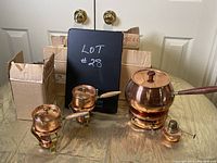 Set of one large and two small copper fondue warmers on a table with cardboard boxes behind.