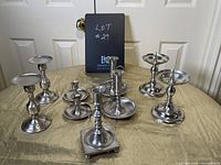 Photo showing all 8 pewter candle holders arranged on beige cloth background with door in background.
