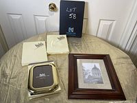 Photo showing three brass photo frames still boxed and one large wooden photo frame placed on a satin fabric surface in front of white doors.