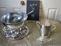 Shows the punch bowl with ladle seated inside, six goblets arranged on the matching tray below, and the ice bucket with handles to the right on a golden textured cloth.