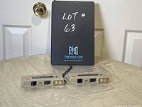 Pair of Stylite pocket cameras shown side by side with a black binder behind them showing lot number. One camera has a string handle attached.