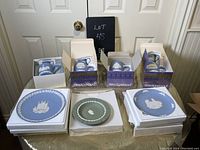 Photo of all four boxed Wedgwood Christmas mugs and three plates (including one sage green Jasperware) displayed on a table.