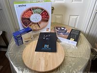 Lot displayed on round table with all items arranged: wooden segmented veggie and dip bowl in box, acrylic butter dish box, cheese board box, and wooden lazy susan.