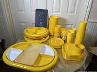 Full view of yellow plastic dish set on table showing trays, plates, bowls, and cups.