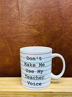 Coffee cup with 'Don't Make Me Use My Teacher Voice' text shown from side view, details of print and handle visible