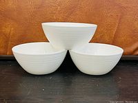 Three white ceramic bowls arranged in a pyramid stack showing ribbed texture on the exterior.
