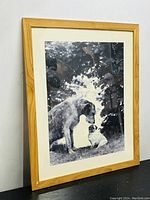 Framed black and white photo showing a large and small dog interacting, with wooden frame and glass.
