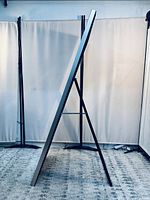 Side view of large full-length mirror standing on rear black foldable support stand, angled against a fabric backdrop.
