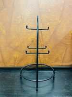 Front view of a black metal mug holder with multiple hooks and circular base against a textured brown background.