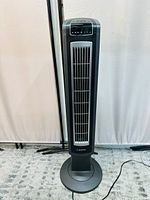 Front view of the Lasko black tower fan showing vertical air vents and electronic touch control panel at the top.