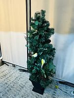 Photo of small green artificial Christmas tree with pine needles, pinecones, and yellow bird decorations on a black base