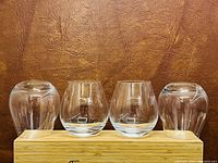 Front view of four shorter curved glasses on a bamboo tray against a brown leather textured background