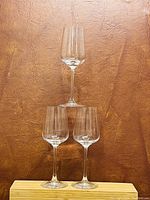 Three clear wine glasses arranged in a triangular formation showing their shape and size against a brown textured background.